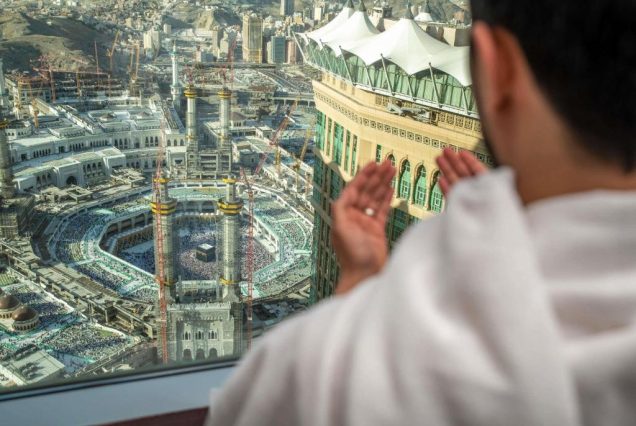 رجل يؤدي الدعاء من شرفة فندق فيرمونت مطلة على الحرم المكي مع ظهور الكعبة المشرفة في الخلفية داخل المسجد الحرام الكعبة المشرفة.